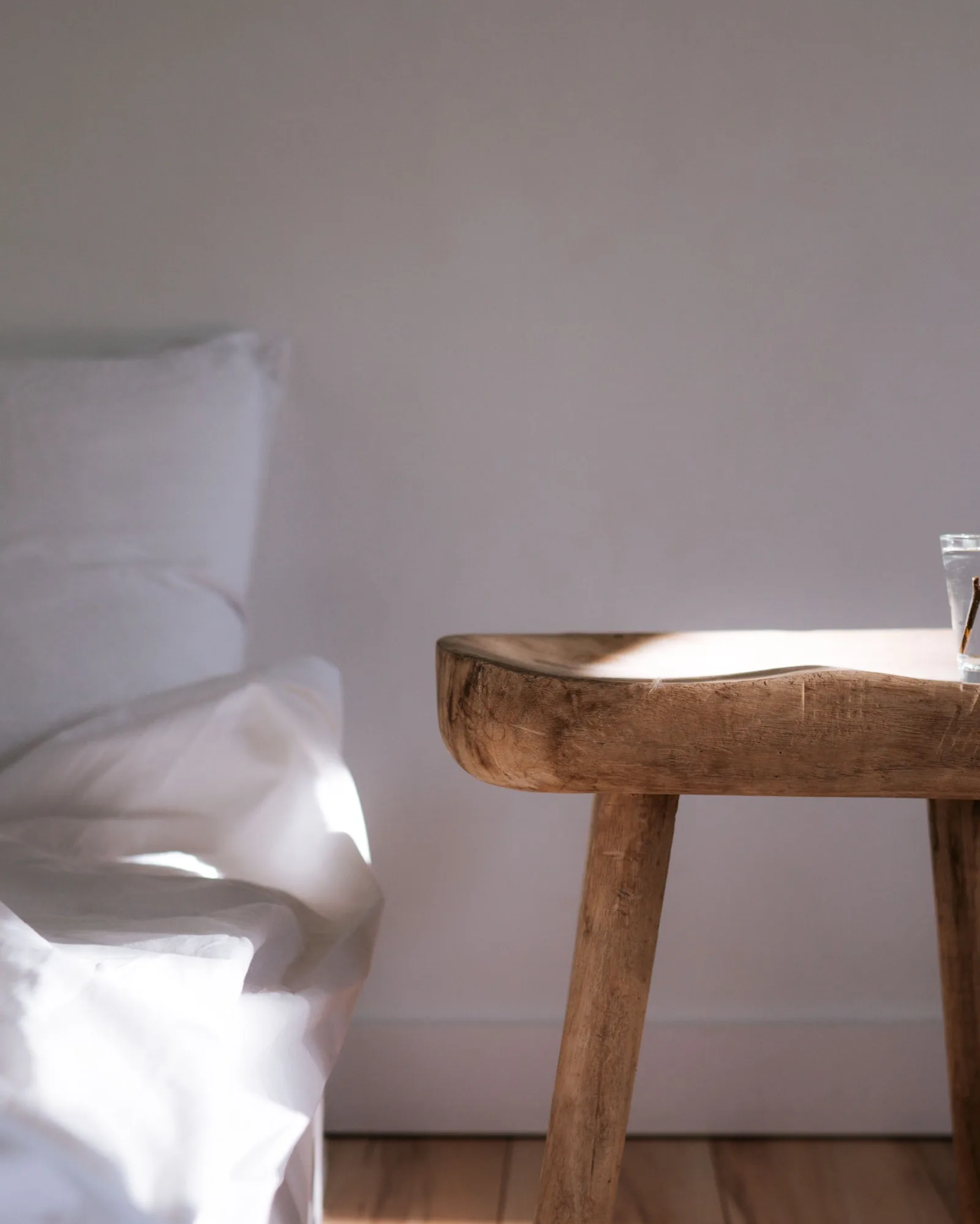 Chambre baignée de lumière au réveil, linge de lit blanc et table de chevet en bois avec une plante